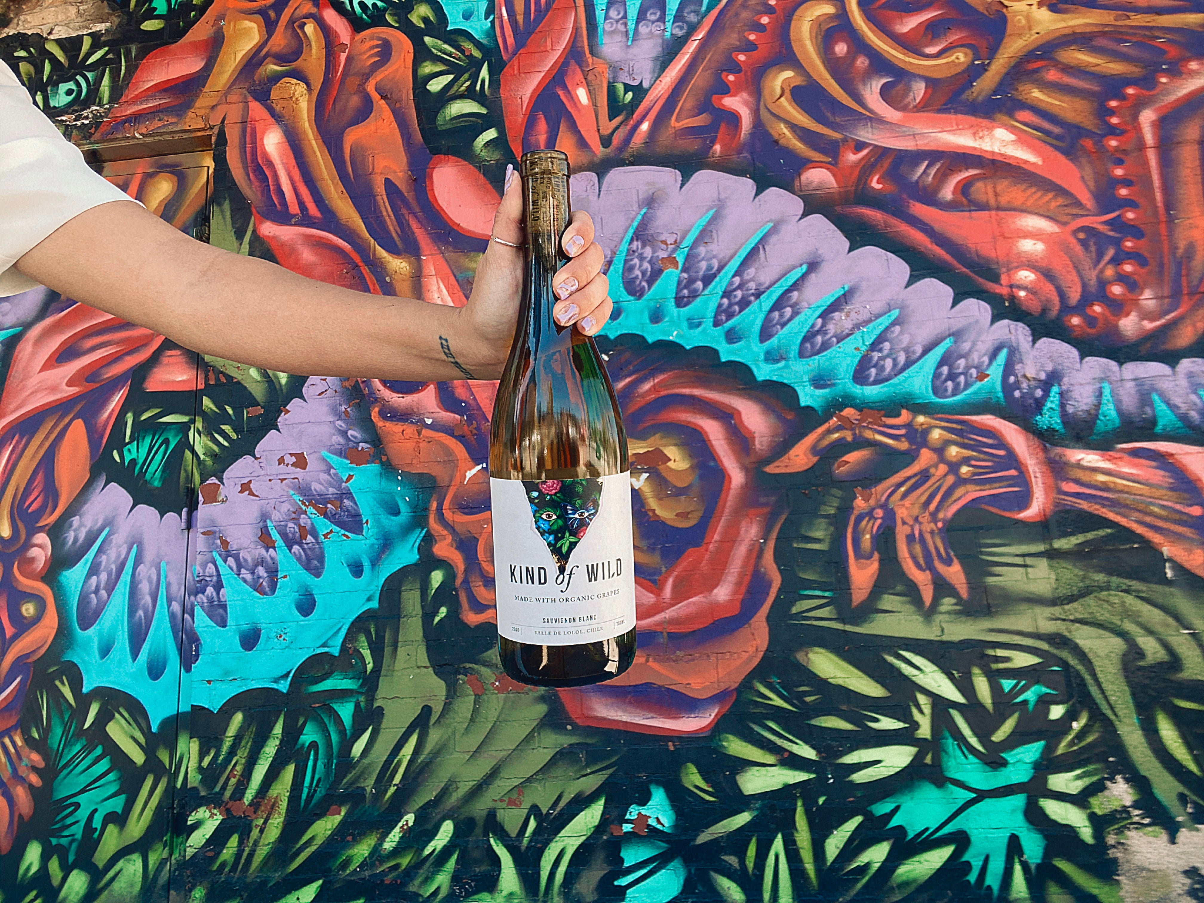 Person holding a bottle of 'Kind of Wild' wine against a colorful mural background